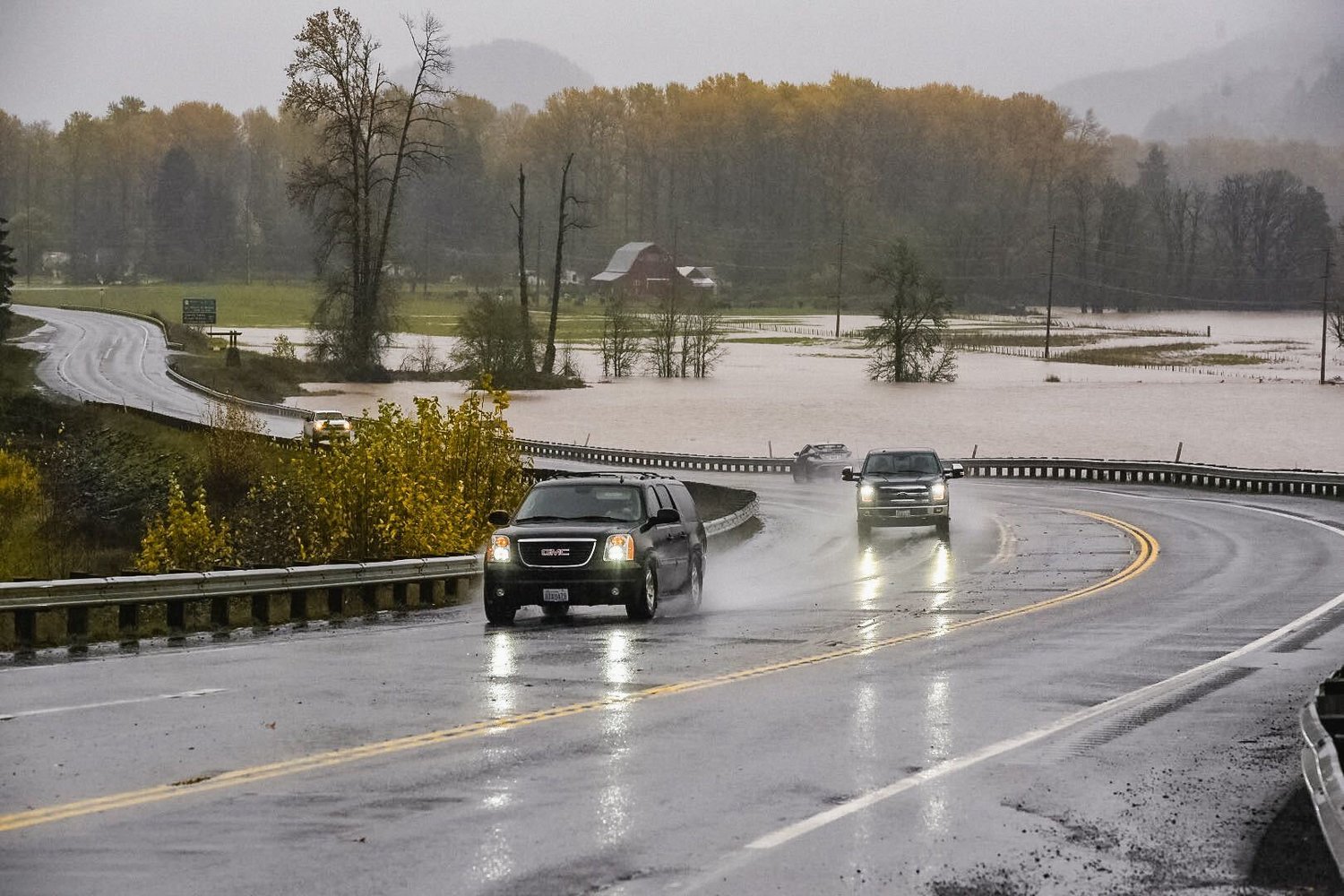 Vehicles drive on Highway 12 in Randle as floodwaters flow from the Cowlitz River along nearby fields.